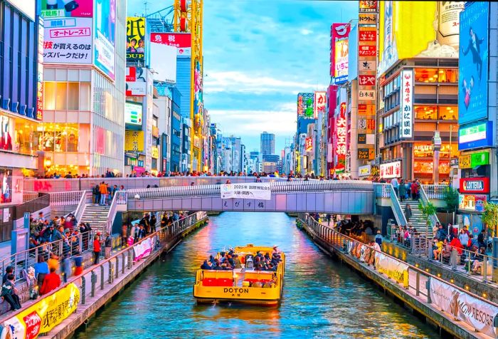 A yellow ferry glides elegantly beneath a bridge, while the lively riverbanks buzz with pedestrians amid colorful advertisements.