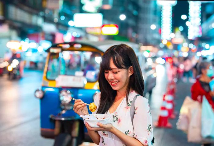 A young woman enjoying a bowl of street food at a bustling night market.