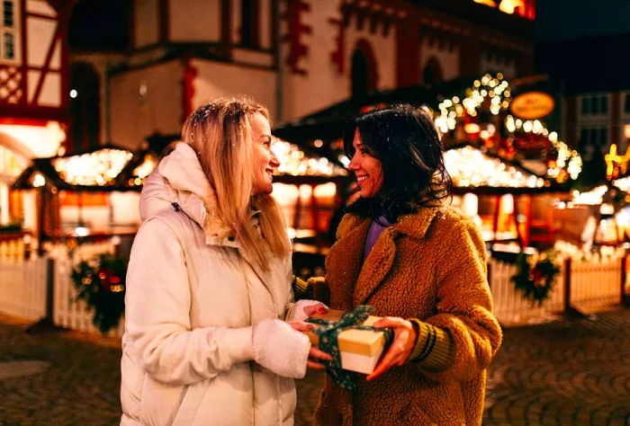 Two women in winter jackets beam as they hold a beautifully wrapped gift.