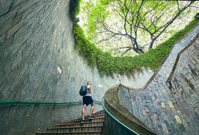 A male traveler with a backpack ascends a spiral staircase.