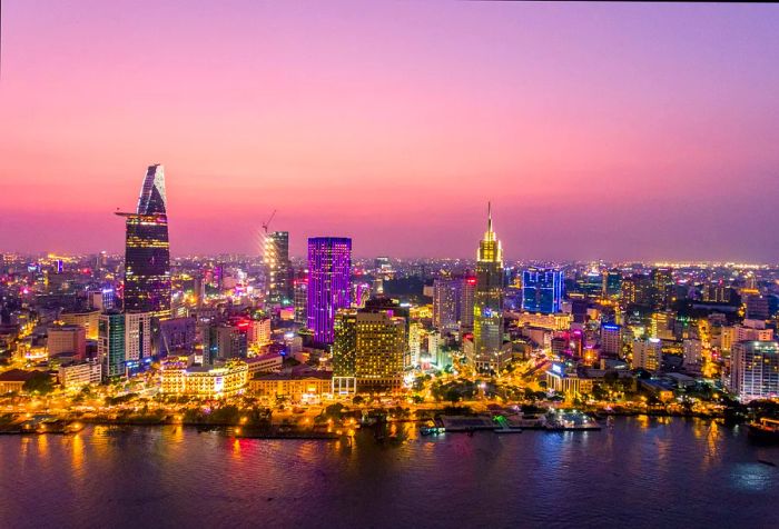 A dense cluster of buildings sprawls across a vast valley, illuminated at night beside a wide river.