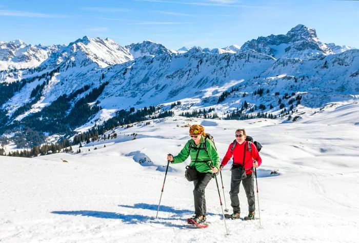 A pair of hikers navigating a snowy terrain with frosty mountains looming in the background.