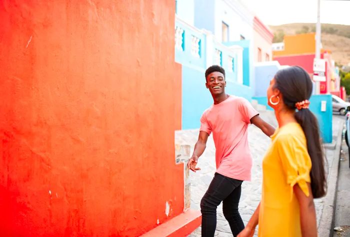 A young, happy couple stands on a sidewalk lined with vibrant, colorful buildings.