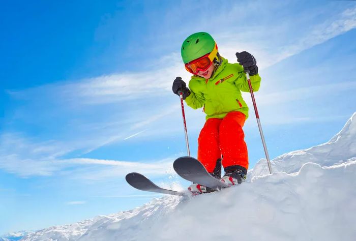 A cheerful little girl, bundled up in warm clothing, glides gracefully across the snow beneath a clear blue sky.