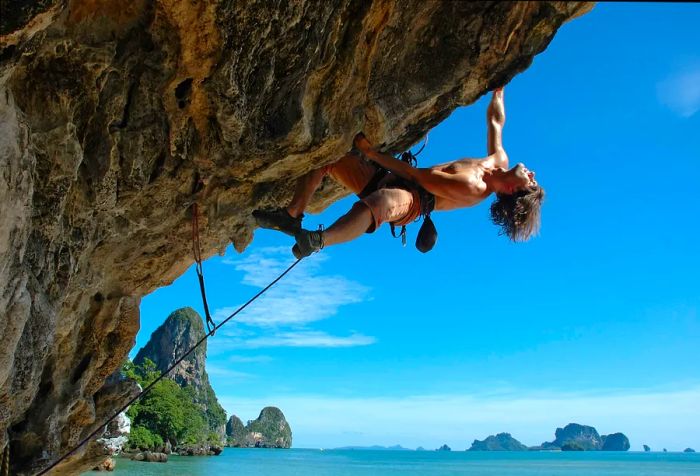 A rock climber grips an overhanging rock face, secured by safety ropes.