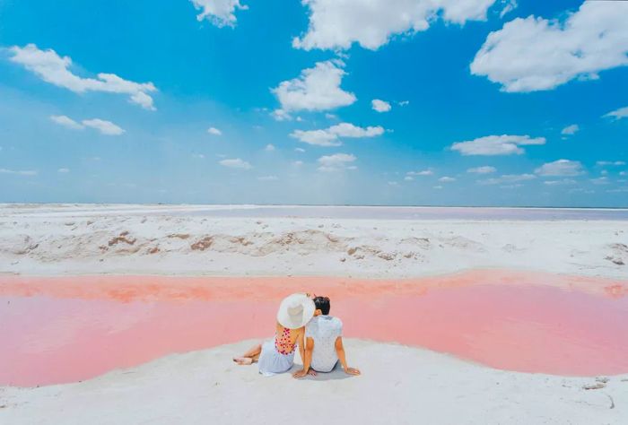 A charming couple relaxes on the white shores of a breathtaking pink lagoon.