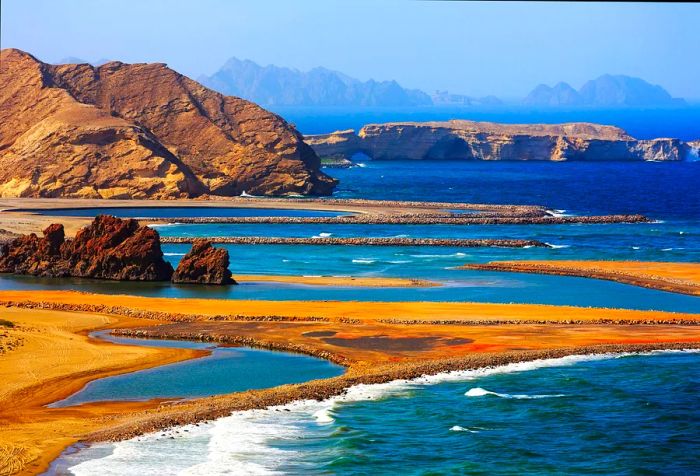 The azure sea cascades over the golden sandy beach, sheltered by rugged rock formations.