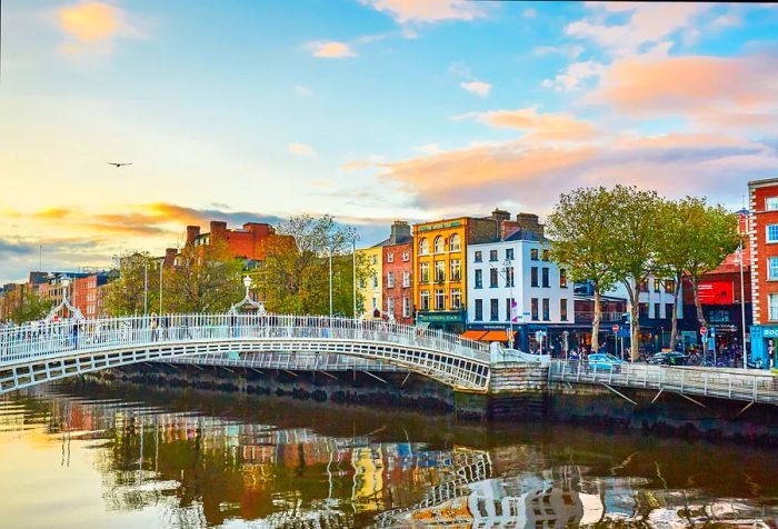 A charming iron footbridge spanning a river, framed by vibrant buildings in the background.