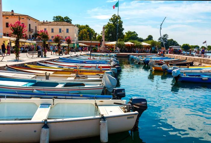 People stroll along a harbor filled with moored boats.