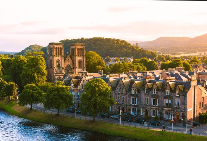 A brick church with twin spires overlooks the terraced buildings lining a serene river.