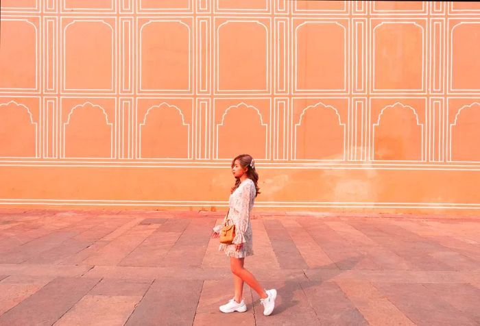 A young woman walks alongside the Painted Pink Wall of the Jaipur City Palace in Rajasthan, India.