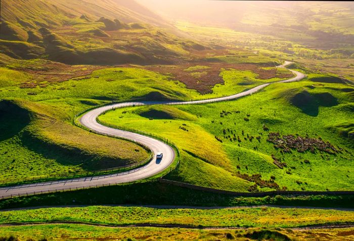 Bathed in golden light, the hills of the Peak District in Derbyshire reveal a winding road leading into the Edale Valley during early summer.