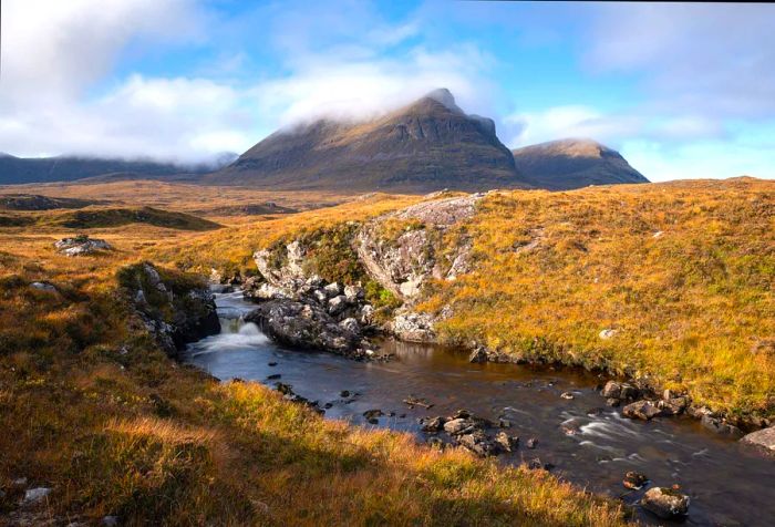 A scenic view of a tranquil river in the Highlands with a mountain shrouded in clouds in the backdrop.