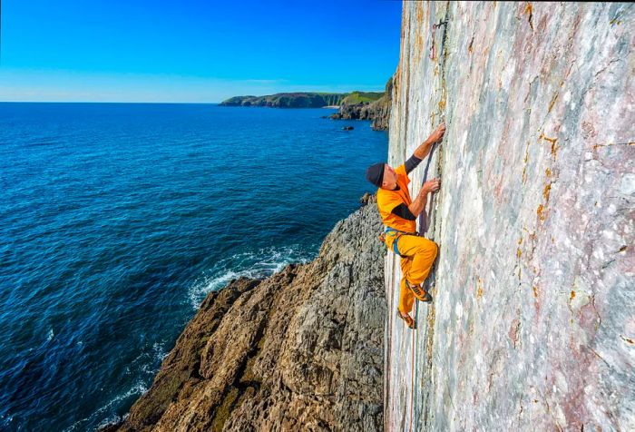 A man ascends a rocky cliff next to the sea.