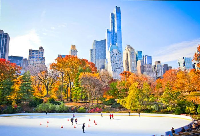 Skaters glide across a park's ice rink, framed by vibrant autumn foliage and the backdrop of modern skyscrapers.