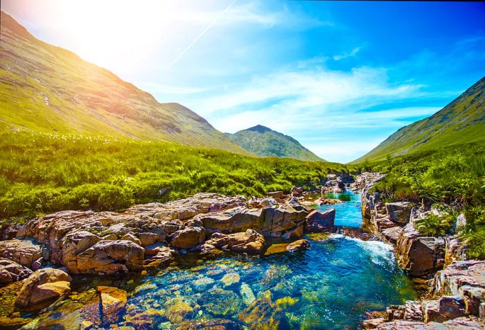 Crystal-clear waters flow over a rocky stream that winds between the lush valleys.