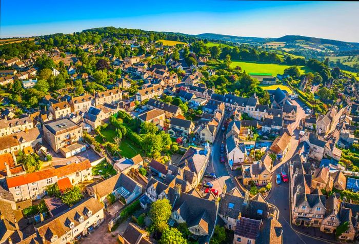 A picturesque urban landscape featuring limestone houses, small green spaces, and a large open field.