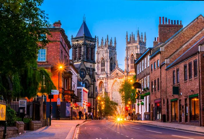 In the distance, you can spot the York Minster cathedral, alongside a street adorned with brick houses and glowing lampposts.