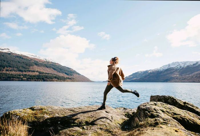 A woman jogs among the rocks with a view of Loch Lomond in Scotland.