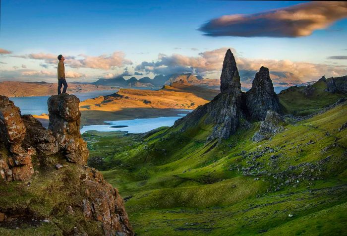 A man gazes skyward while standing on a rocky pillar, surrounded by rugged plateaus and rocky pinnacles.