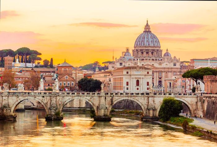 An arch bridge spans a serene river, with a distant domed church silhouetted against an orange-hued sky.