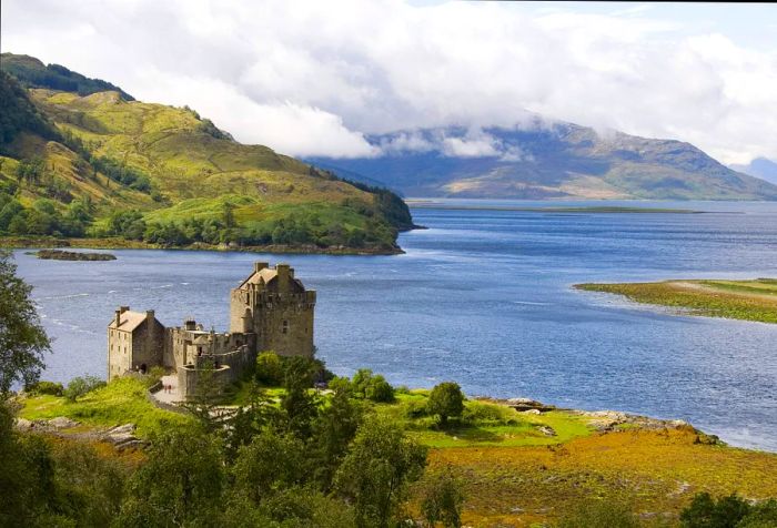 Eilean Donan is an impressive castle with curtain walls, perched on a hill and overlooking a lake with stunning views of the surrounding mountains.