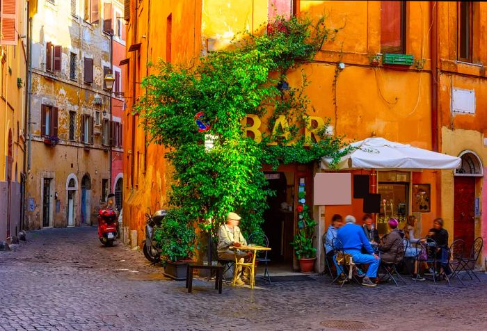 People enjoy drinks in an outdoor bar next to a narrow street lined with traditional townhouses.