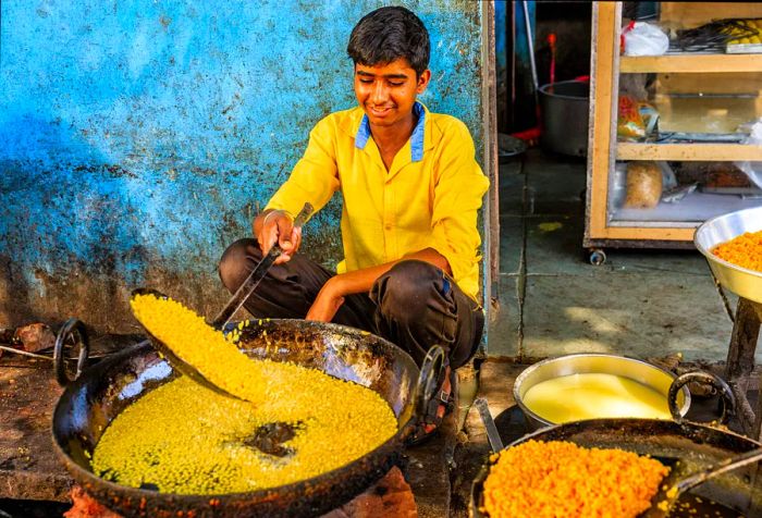 A young Indian boy in bright yellow attire skillfully prepares delicious street food.