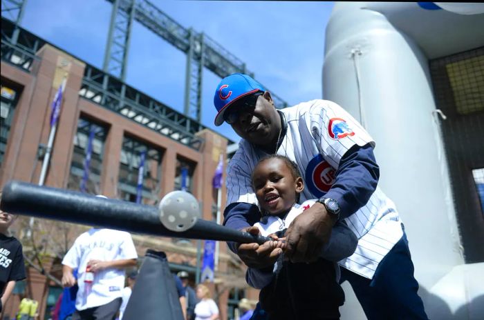 A young boy practices swinging a baseball bat with his grandfather outside Coors Field in Denver, Colorado