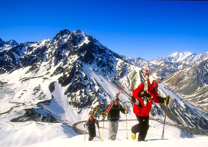 A group of skiers trekking for fresh powder with their skis slung over their shoulders in the backcountry of Portillo, a renowned winter sports destination in the Andes, Chile.