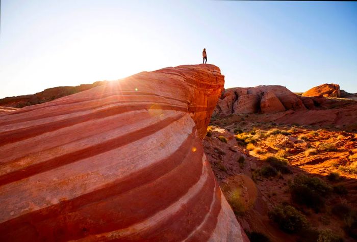 A person stands at the brink of a stunning rock formation, featuring mesmerizing streaks and lines, gazing out over the vast desert expanse.