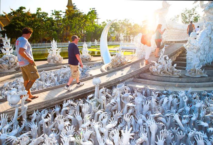 Visitors cross a bridge adorned with hundreds of reaching hands as they arrive at the sunlit white temple.