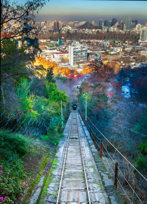 A tramway winds through the forest atop San Cristobal hill in Santiago, Chile, with the city sprawling out in the background.