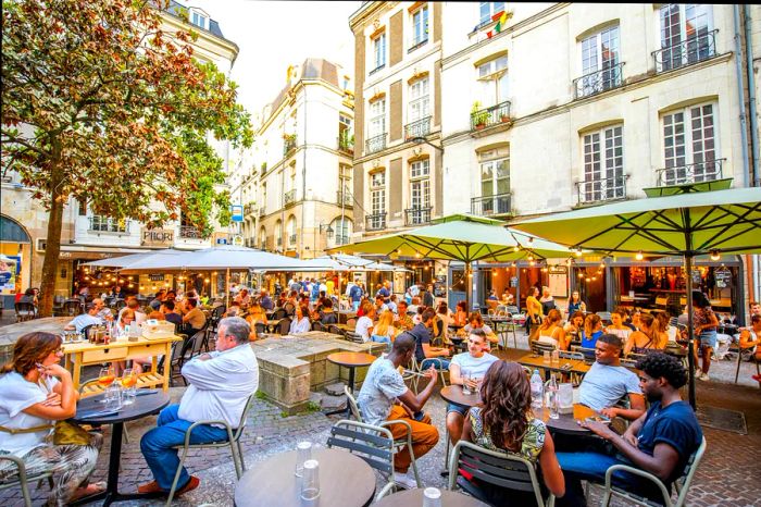 A vibrant street scene filled with cafes and restaurants bustling with patrons in Nantes' historic old town, France.