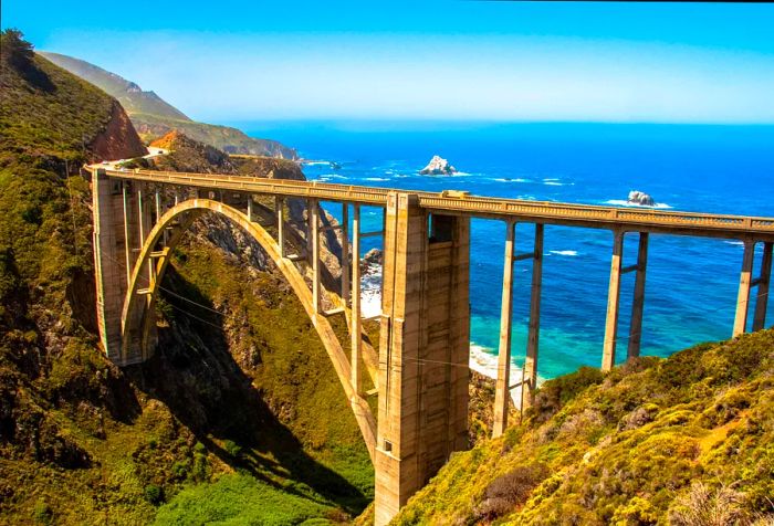 A towering arch bridge spanning a ravine between two cliffs, overlooking the ocean.