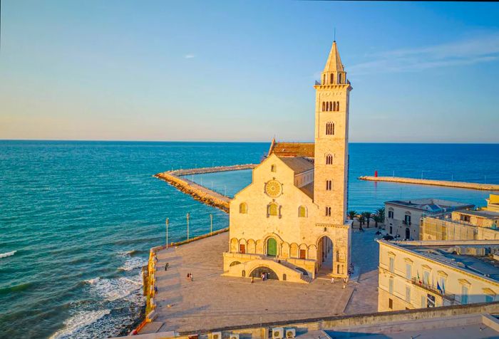 A Romanesque church featuring a bell tower nestled in a cobblestone square by the coast.