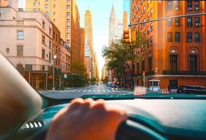 The driver's perspective from inside a car at an intersection, with tall city buildings lining the street.