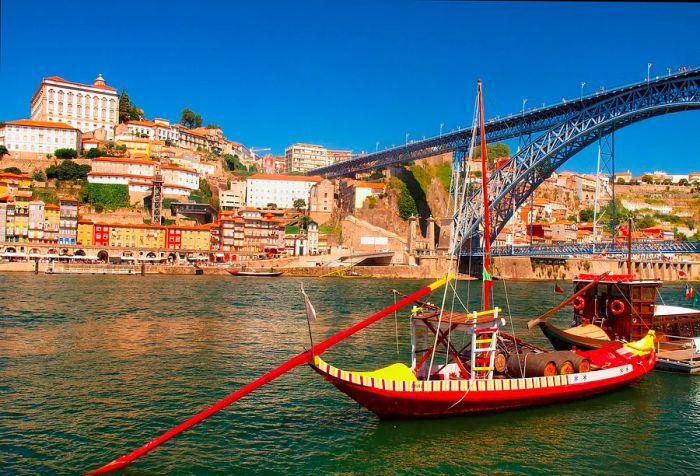 A rabelo boat approaches the double-deck metal arch bridge spanning the river, leading to a hillside of tall buildings.