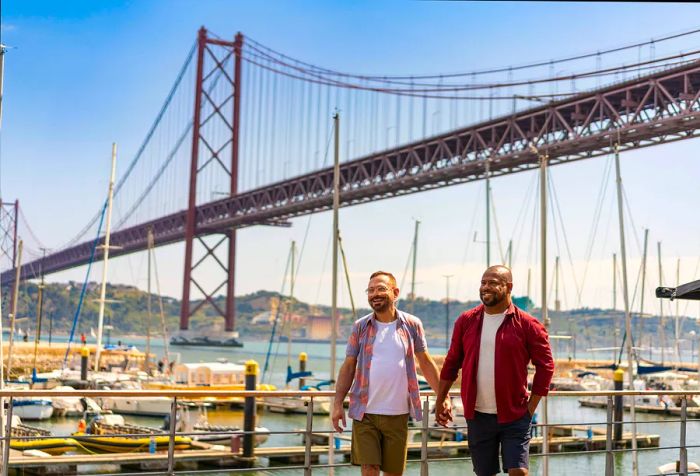 A cheerful couple walks hand in hand along the promenade, framed by a bustling harbor and an iconic bridge spanning the sea.