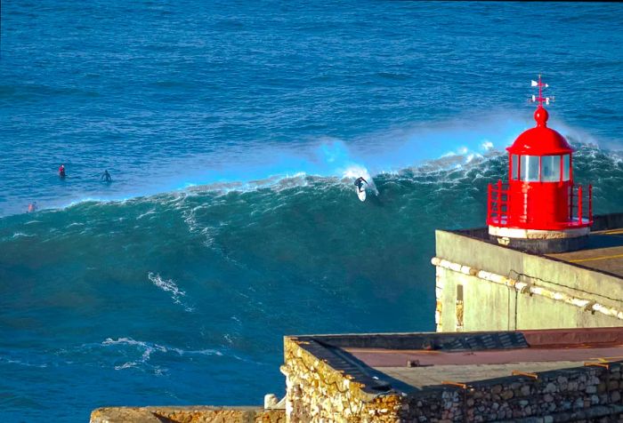 A red lighthouse stands sentinel over the ocean, where surfers catch the rolling waves.