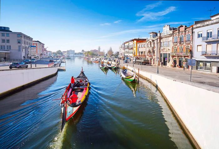 A boat glides through a canal lined with moored vessels, framed by vibrant buildings.