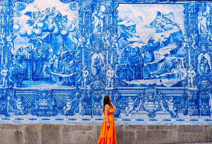 A woman in an orange dress admires the intricate traditional azulejo tiles in a charming city.