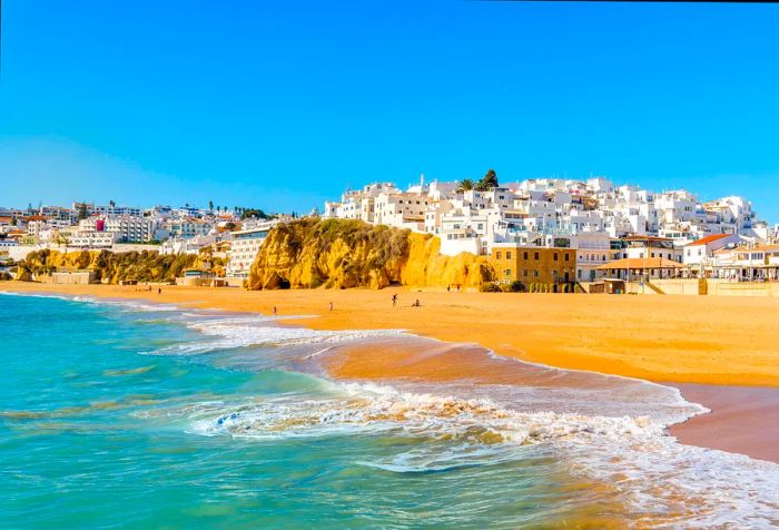 A picturesque sandy beach adorned with white houses against a clear blue sky.