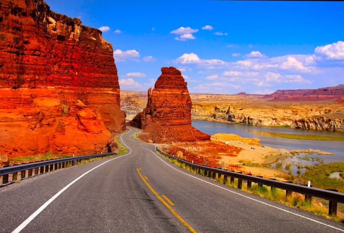 A desolate road winds between stunning red and orange sandstone canyons, offering picturesque riverfront views.