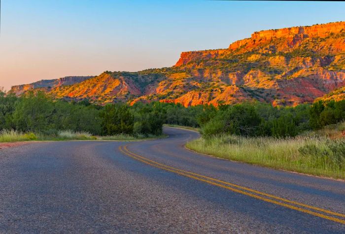 A meandering road flanked by sandstone hills and mountains.