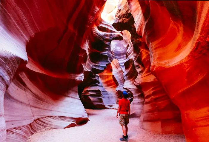 A visitor stands within Antelope Canyon, looking up through a natural opening in the sandstone, surrounded by a dreamlike display of intricate textures and shifting light.