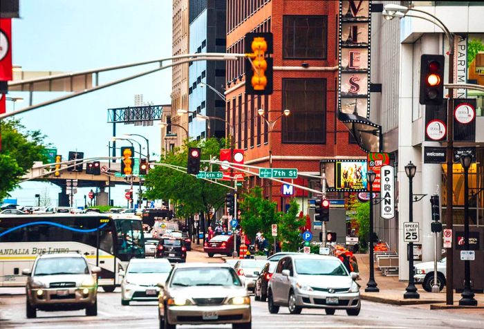 Vehicles navigate a bustling street filled with directional signs, traffic lights, and towering buildings.