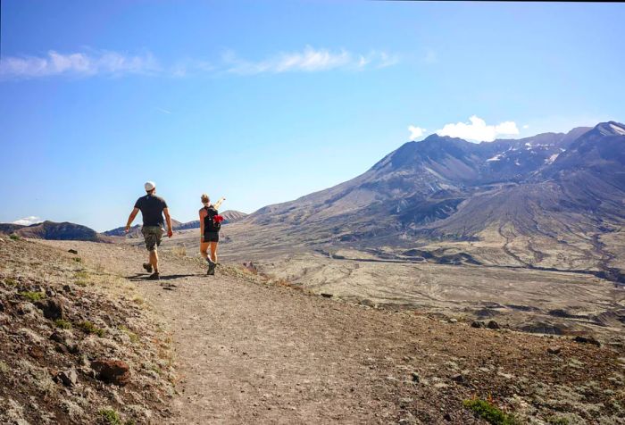 Two individuals hike up a volcanic mountain on a bright summer day.