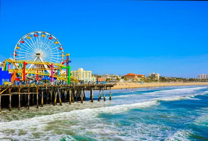 A vibrant pier featuring an amusement park on a beach, set against a backdrop of urban architecture.