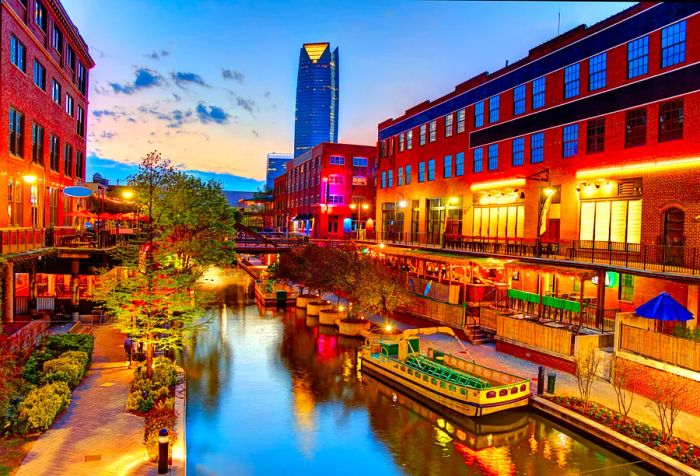 A nighttime scene of a serene canal with a moored tourist boat lined by trees and shops.